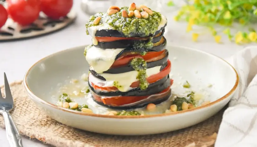 Deliciosa milhoja de berenjena con tomate, mozzarella fundida y pesto, coronada con piñones. Un plato ligero y sabroso.