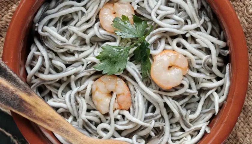 Deliciosas recetas con gulas y gambas, servidas en cazuela de barro con perejil y cuchara de madera.