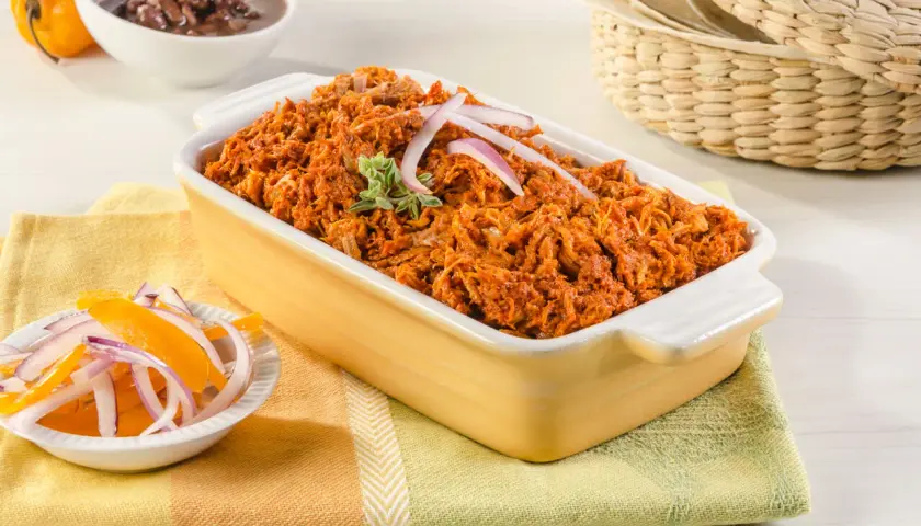 Cochinita pibil, un platillo yucateco de cerdo deshebrado en achiote, servido con cebolla morada y naranja.
