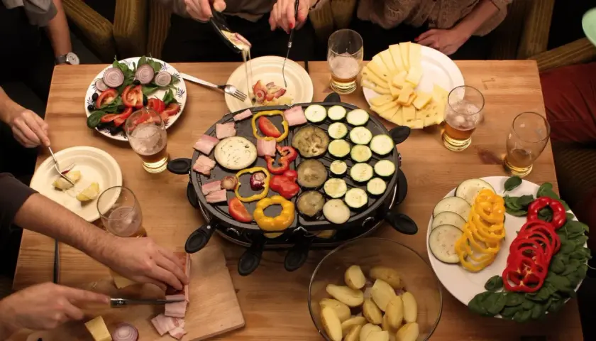 Mesa con raclette, queso, verduras y patatas. ¡Ideas raclette para una cena divertida!