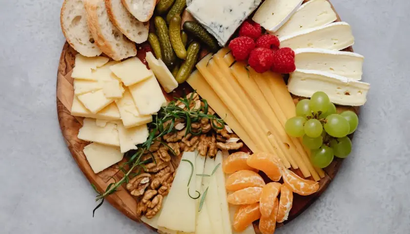 Tabla de quesos como hacerla: variedad de quesos, uvas, frutos rojos, nueces, pepinillos y pan.