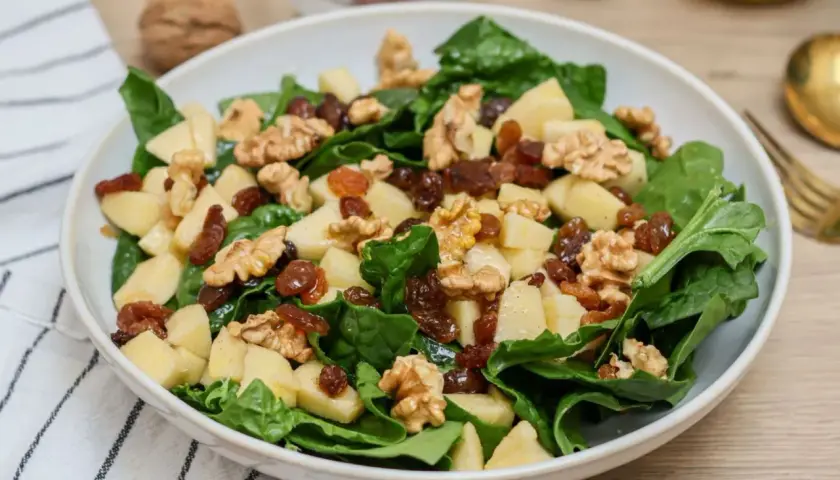 Deliciosa ensalada de espinacas con trozos de manzana, pasas y nueces. Una combinación crujiente y dulce.