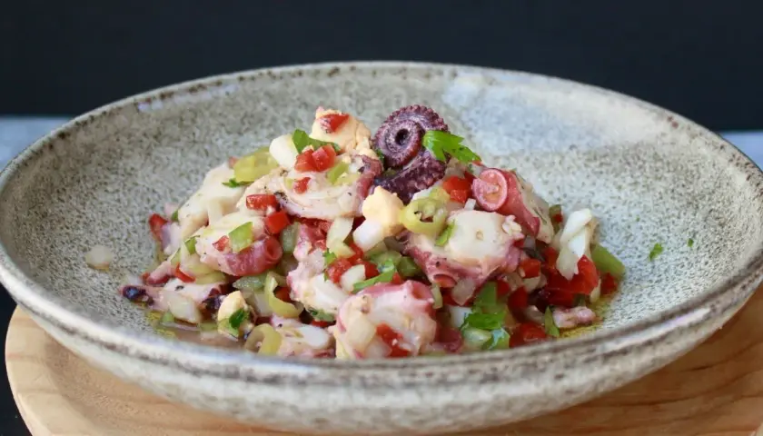 Un refrescante salpicón de pulpo con pimientos, cebolla y aceitunas, servido en un cuenco rústico.