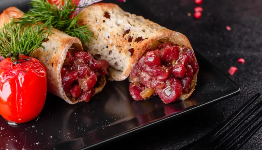 Delicioso steak tartar servido en pan tostado, acompañado de tomates cherry asados y eneldo fresco.