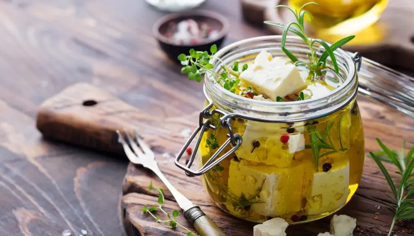 Queso en aceite de oliva, con hierbas aromáticas y granos de pimienta, listo para disfrutar.