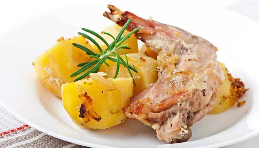 Conejo al horno jugoso con patatas asadas y romero fresco. Un plato tradicional y delicioso.