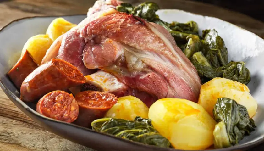 Un plato generoso de lacon con grelos, acompañado de chorizo y patatas cocidas, listo para ser disfrutado.
