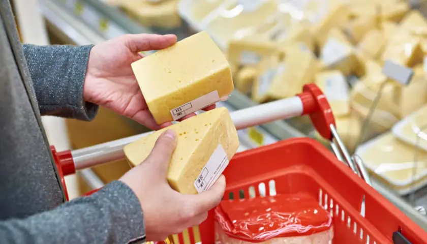 Manos sostienen trozos de queso cheddar, buscando opciones sin lactosa en el supermercado.