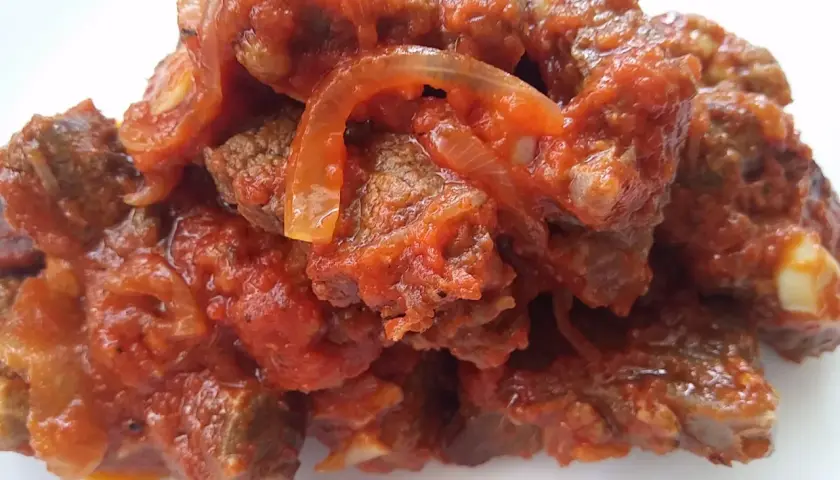Un plato humeante de carne con tomate y cebolla, cocinado a fuego lento hasta que la carne esté tierna y la salsa espesa.