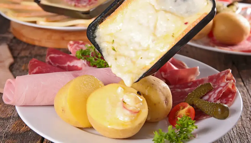 Raclette, comida típica de Suiza, con queso derretido, patatas, embutidos y pepinillos.