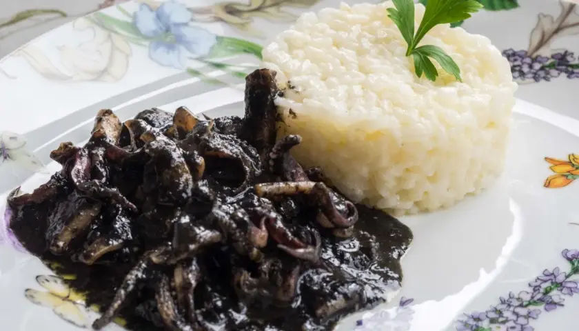 Deliciosos calamares en su tinta, servidos con arroz blanco y decorados con perejil fresco.