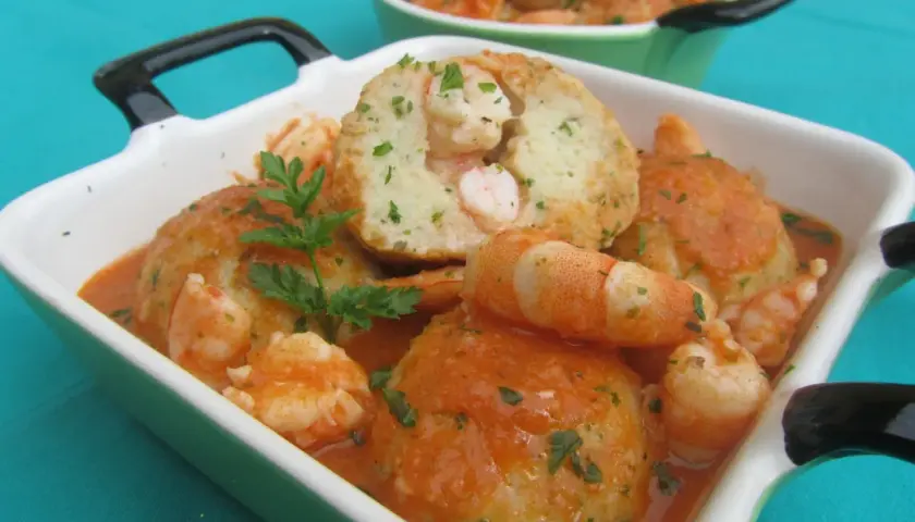 Deliciosas albóndigas de rape con gambas en salsa de tomate, adornadas con perejil fresco.