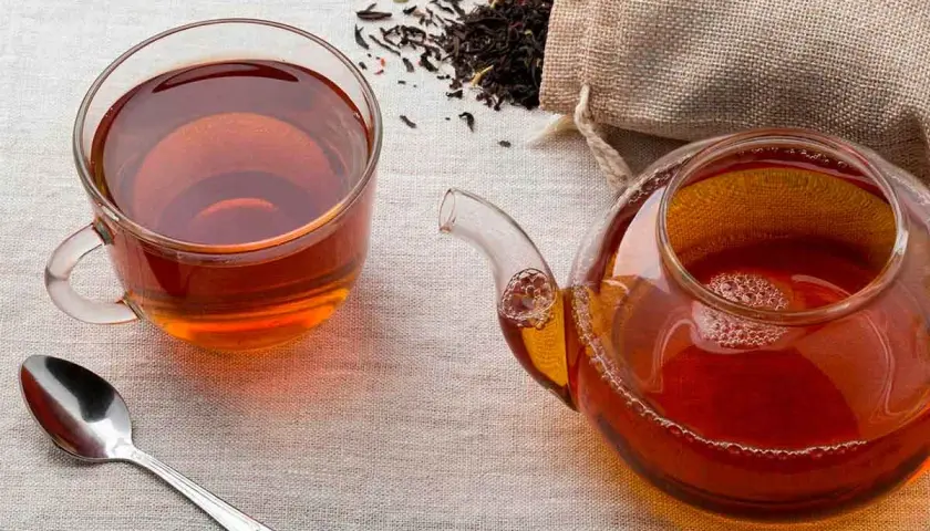 Una taza y tetera de té negro, con hojas secas esparcidas. ¿A que sabe el té negro? A un sabor robusto y reconfortante.