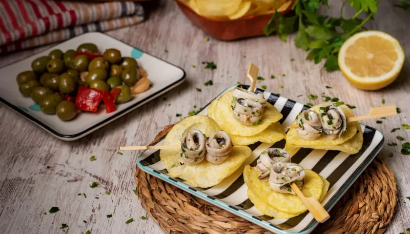 Deliciosas recetas con anchoas: pinchos de anchoas enrolladas sobre patatas fritas, acompañadas de aceitunas y limón.