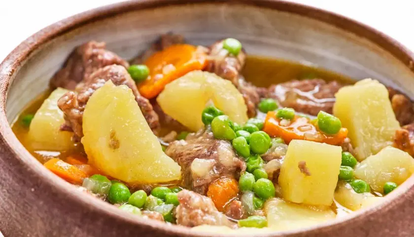Un reconfortante ragú de ternera con patatas, zanahorias y guisantes en un cuenco de barro.