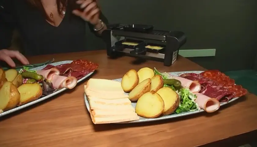 Platos con patatas, embutidos y queso listos para preparar deliciosas recetas raclette en la parrilla.