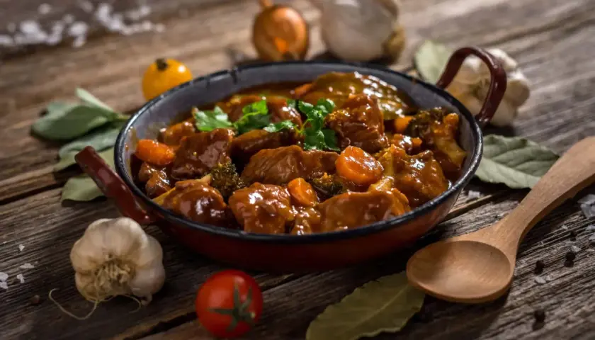 Un delicioso ragú de carne con zanahorias y brócoli en una sartén, acompañado de ajo, cebolla y hierbas.