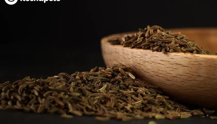 Montón de alcaravea especia cayendo de un cuenco de madera.