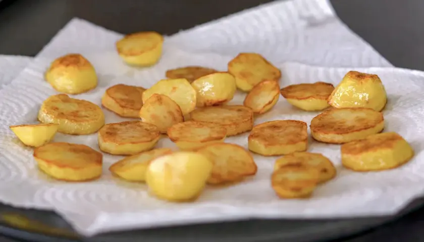 Rodajas doradas de patatas al horno, recién salidas de la sartén y escurriendo el exceso de aceite sobre papel de cocina.