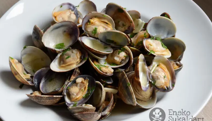 Un plato de almejas a la marinera, recién cocinadas y espolvoreadas con perejil picado.