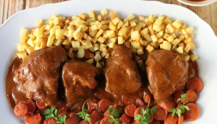 Delicioso jarrete de ternera estofado en salsa, acompañado de patatas fritas y zanahorias.