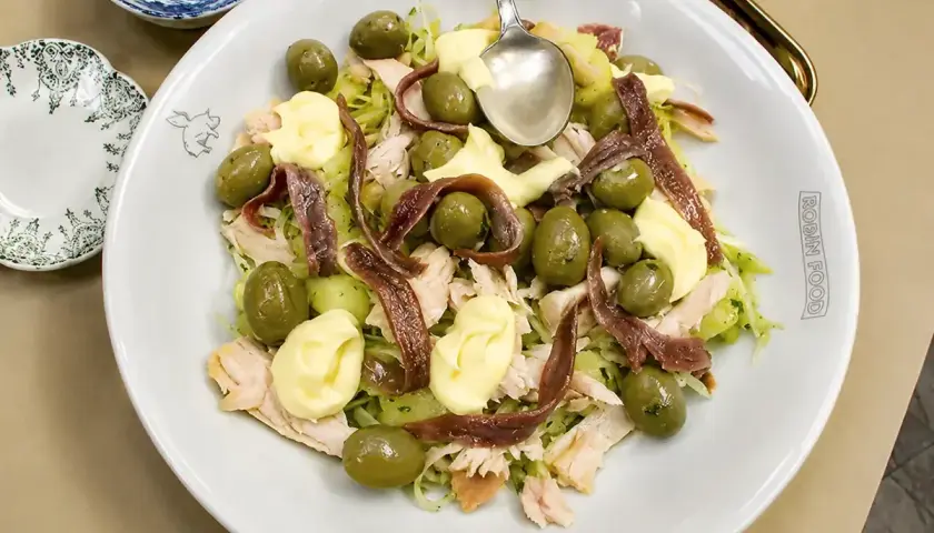 Ensalada fresca con patatas, aceitunas verdes, mayonesa y tiras de anchoas.