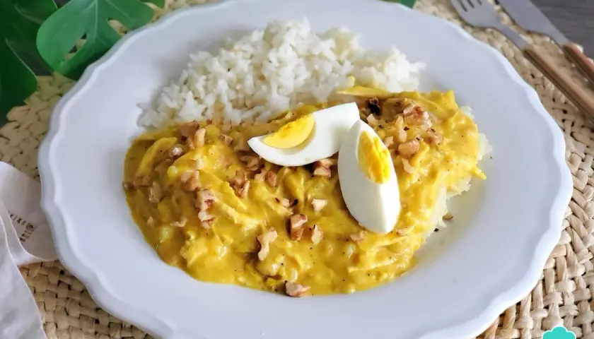 Un plato de aji de pollo cremoso con arroz blanco, huevo duro y nueces picadas.