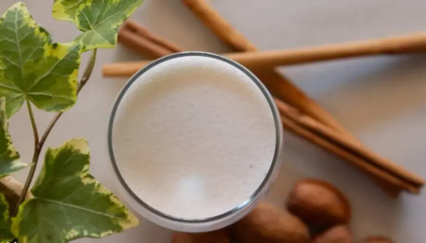 Un vaso de leche espumosa, canela y hojas verdes, recordatorio de los beneficios de la leche de vaca para una vida saludable.