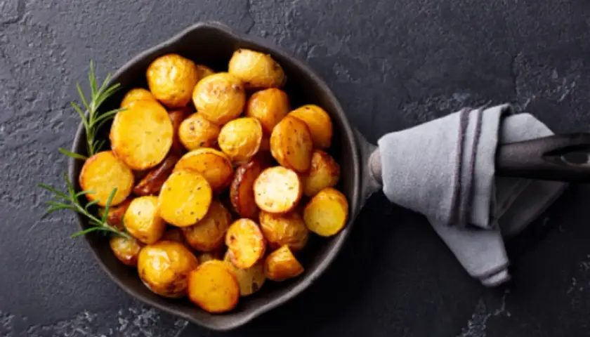 Patatas doradas y tiernas listas para cocer, con romero fresco en una sartén de hierro fundido.