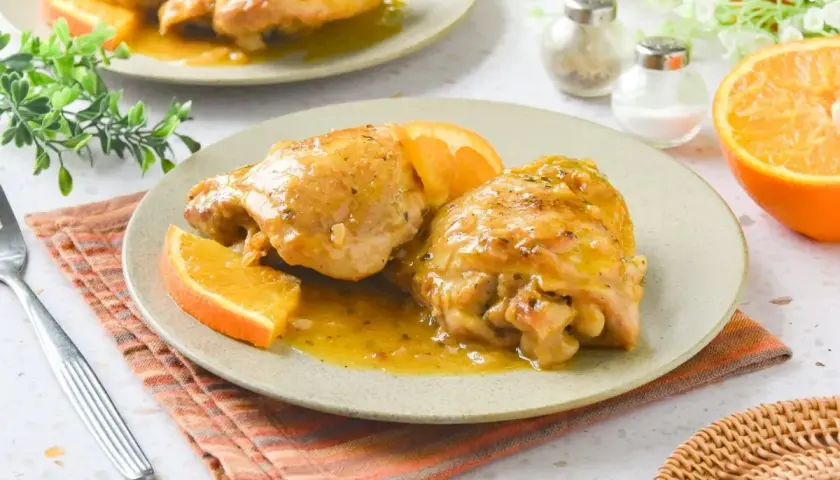 Dos jugosas piezas de pollo a la naranja, bañadas en su salsa y decoradas con gajos de naranja fresca. Un plato delicioso y aromático.