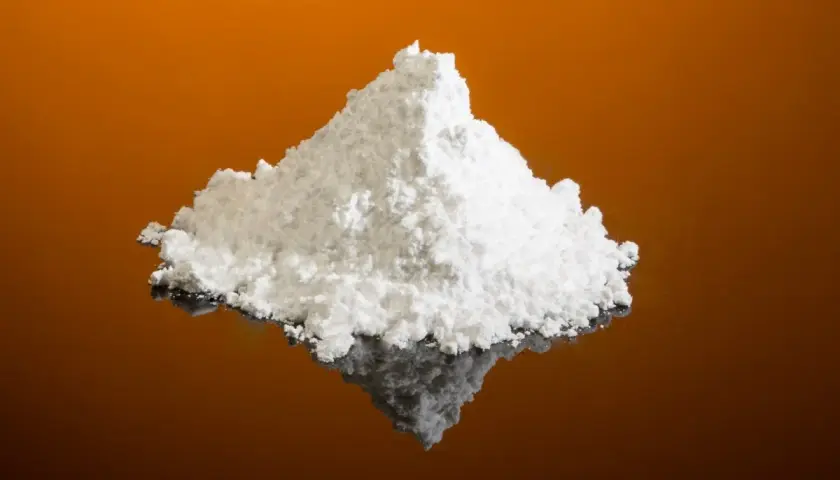 Montículo de polvo blanco fino, que es el cremor tártaro, sobre una superficie reflectante naranja.