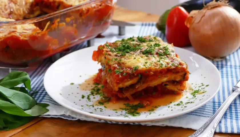 Una porción de parmigiana que es un delicioso plato de berenjenas, salsa de tomate y queso, espolvoreado con perejil fresco.