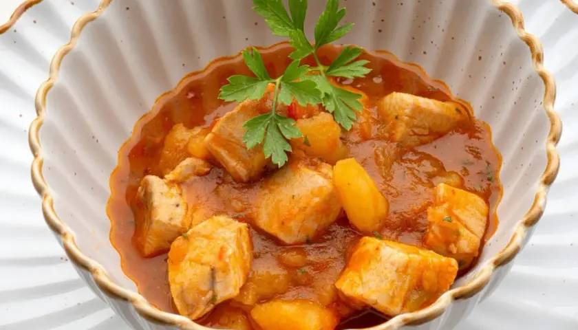Un delicioso marmitako de bonito con patatas y pimientos en una cazuela, adornado con perejil fresco.
