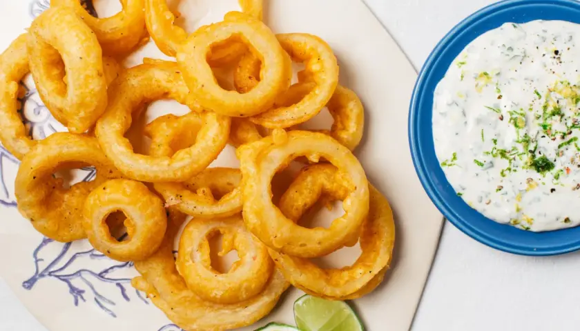 Crujientes aros de cebolla dorados, servidos con una cremosa salsa y gajos de lima. ¡Un aperitivo irresistible!