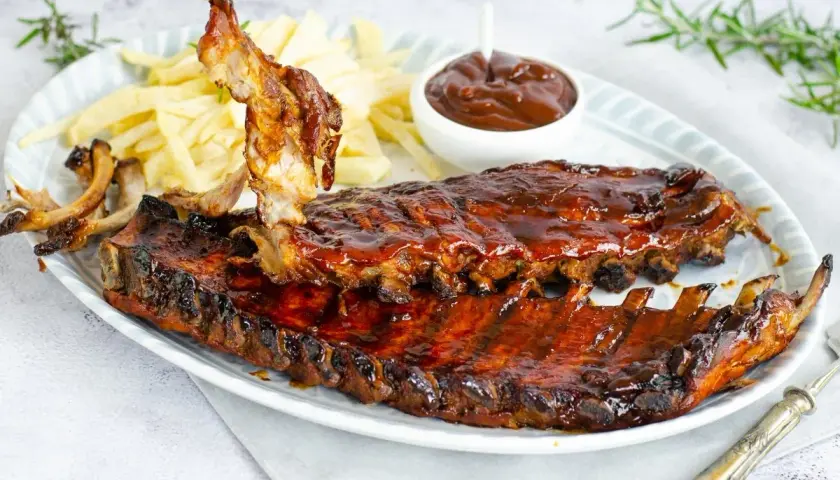 Costillas a la barbacoa jugosas y glaseadas, servidas con patatas fritas y salsa barbacoa. ¡Un festín para los sentidos!
