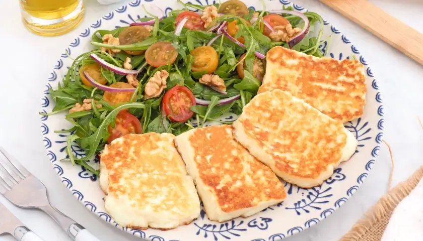 Ensalada fresca con tomates cherry, cebolla morada y nueces, acompañada de trozos dorados de ser halloumi a la plancha.