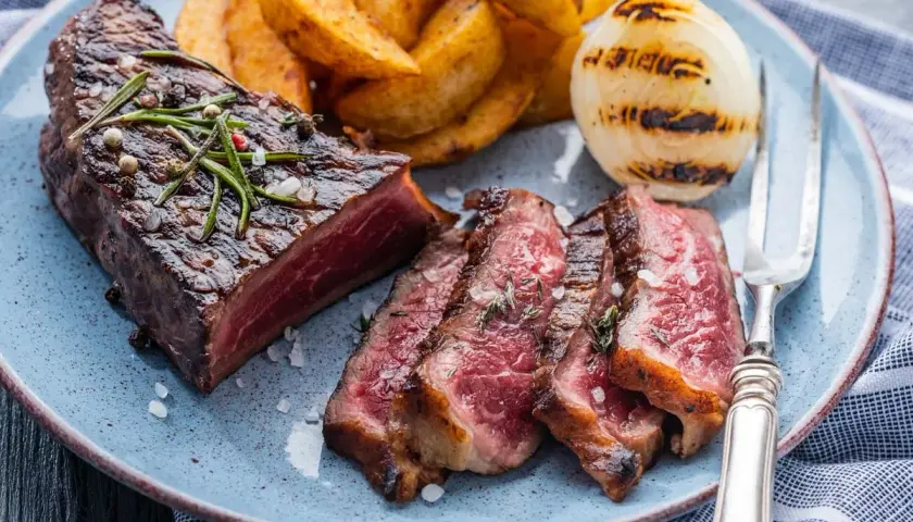 Jugoso entrecot a la plancha, cortado en rodajas, acompañado de patatas gajo y cebolla a la parrilla.