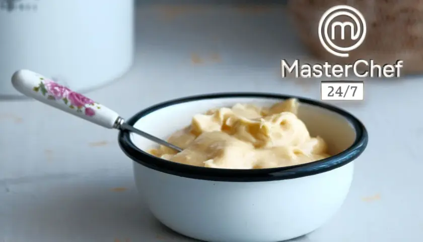 Crema sedosa lista para emulsionar en cocina. Un tazón blanco con borde negro contiene una suave crema amarilla, con una cuchara de mango floral.