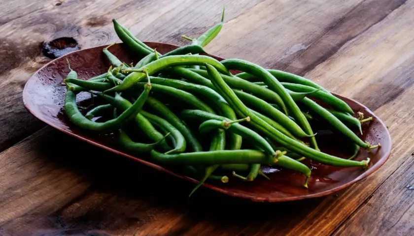 Un plato de judías verdes frescas y vibrantes sobre una mesa de madera rústica, listas para ser cocinadas.