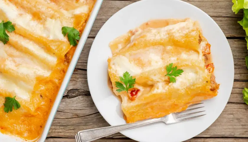 Canelones de atún gratinados, cubiertos de salsa y queso, servidos en un plato blanco con un tenedor.