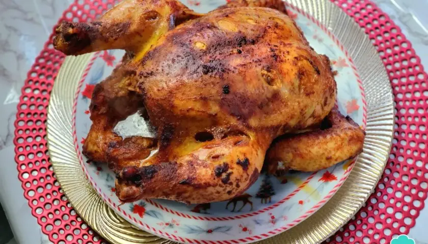 Un jugoso pollo a la brasa, dorado y crujiente, servido en un plato festivo con motivos navideños.