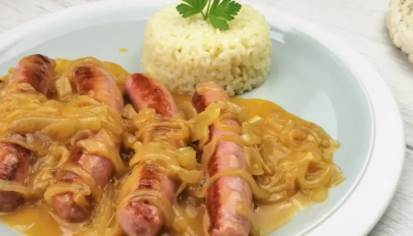 Salchichas al vino con cebolla caramelizada y una porción de arroz blanco, decorado con perejil.