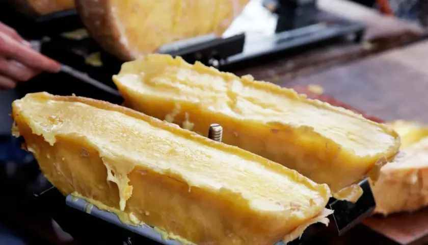 Dos mitades de queso fundido en una máquina para raclette, con el queso derritiéndose y goteando.