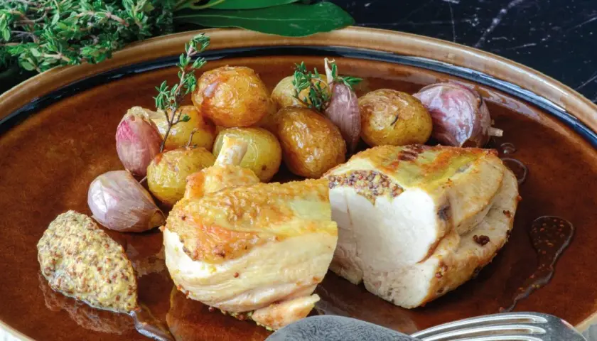 Pollo asado con patatas y ajos, acompañado de una generosa porción de mostaza de grano entero, mostrando varios tipos de mostaza.