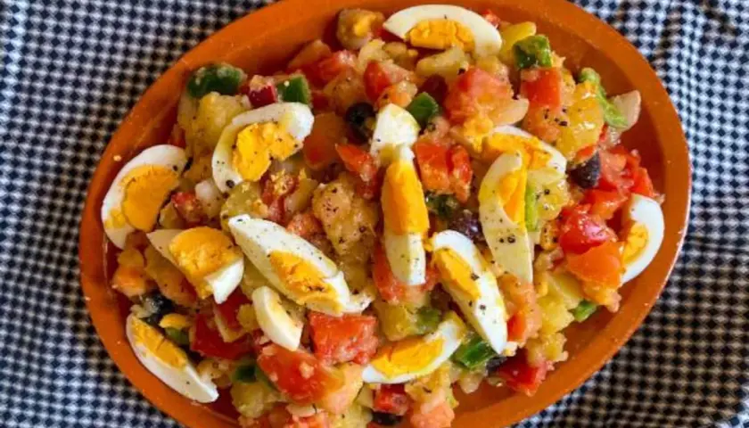 Ensalada campera con patatas, tomate, pimiento, aceitunas y huevos duros, servida en plato de barro.