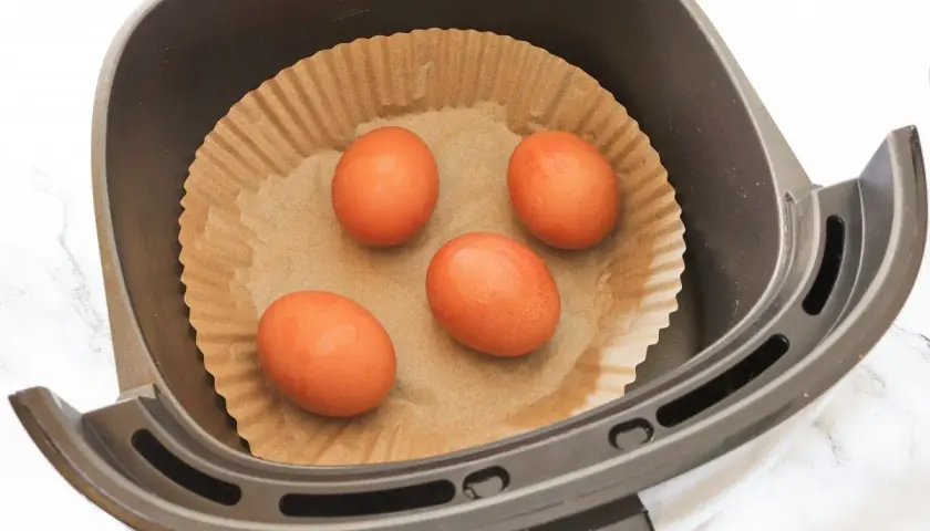 Cuatro huevos listos para convertirse en huevo duro airfryer, colocados sobre papel de hornear en la cesta de la freidora de aire.