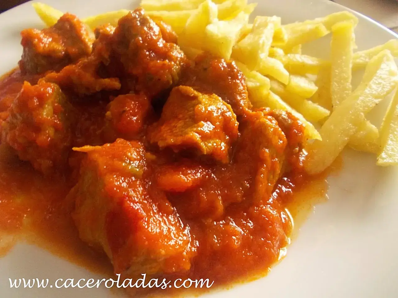 Magro con tomate, jugoso y tierno, servido con patatas fritas crujientes. Un plato casero que reconforta el alma.