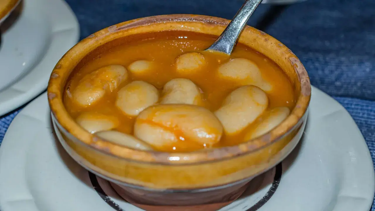 Un cuenco de barro rebosante de judiones de la granja en una salsa dorada, con una cuchara lista para servir.