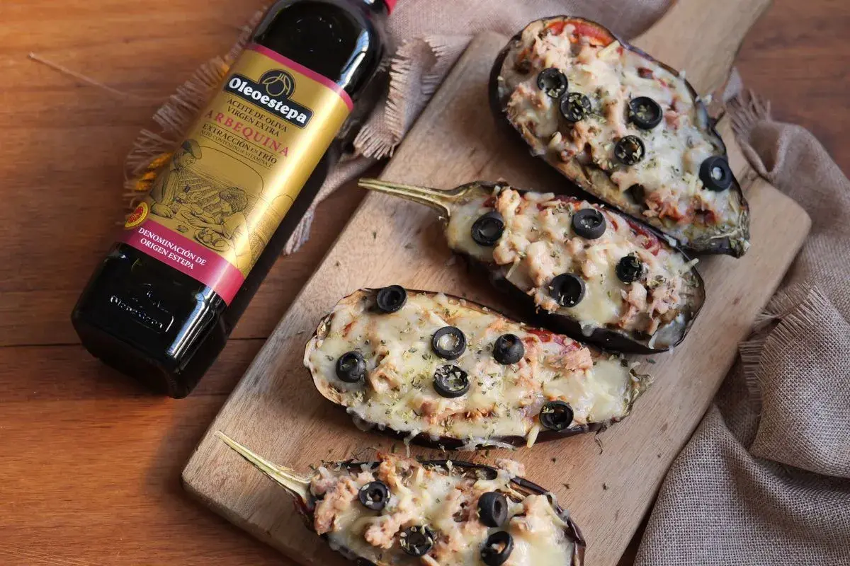 Berenjenas rellenas gratinadas con queso y aceitunas negras, junto a una botella de aceite de oliva virgen extra Oleoestepa.