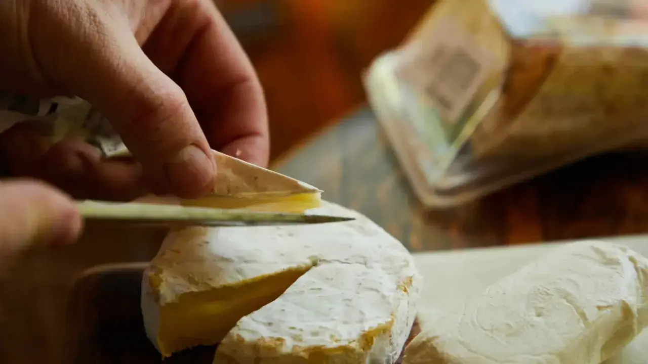 Mano cortando un queso de Tetilla con un cuchillo. Se ve la corteza blanca y el interior cremoso.
